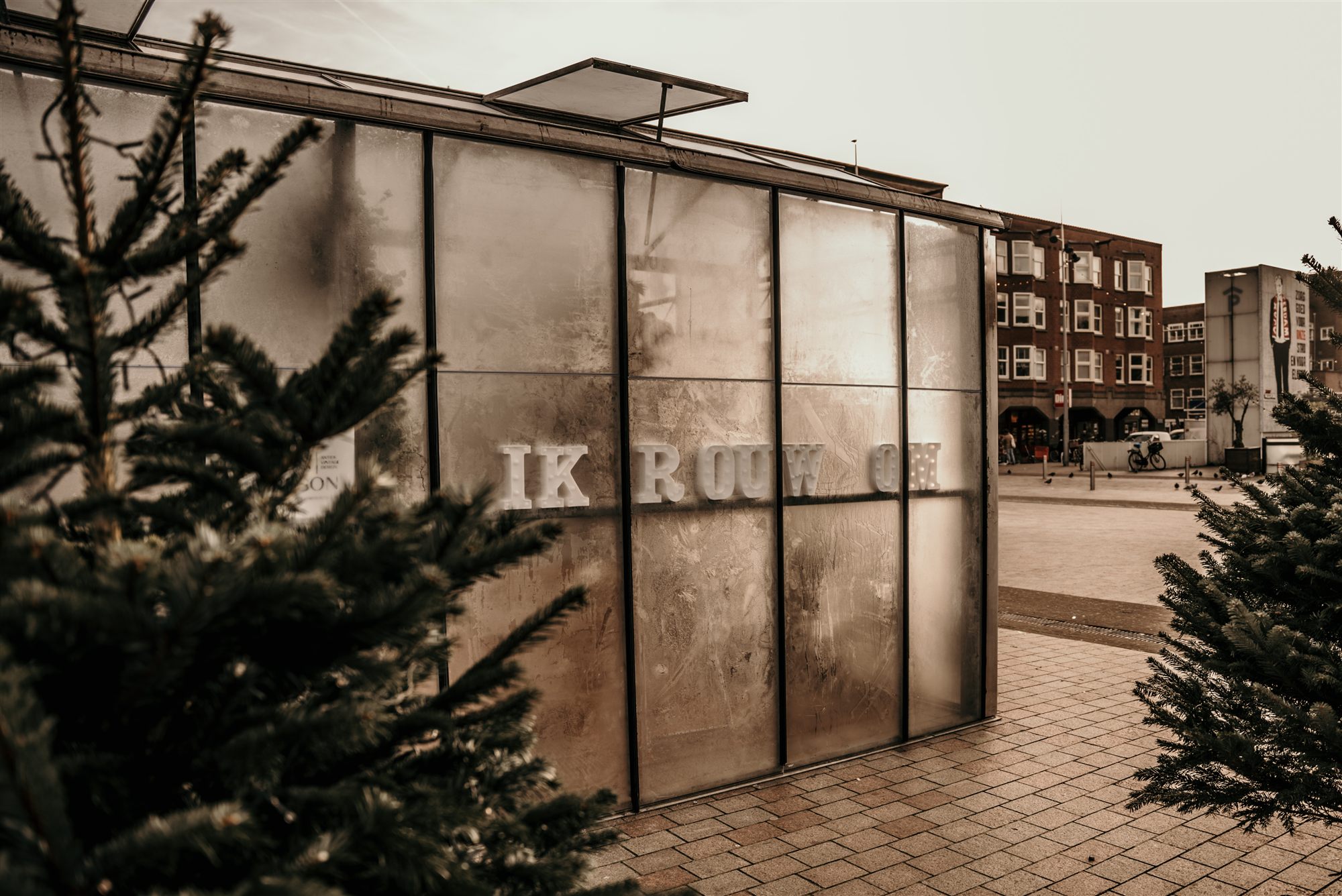 Kas van Rouwen & Vieren met de tekst 'IK ROUW' op het glas, kerstbomen ervoor
