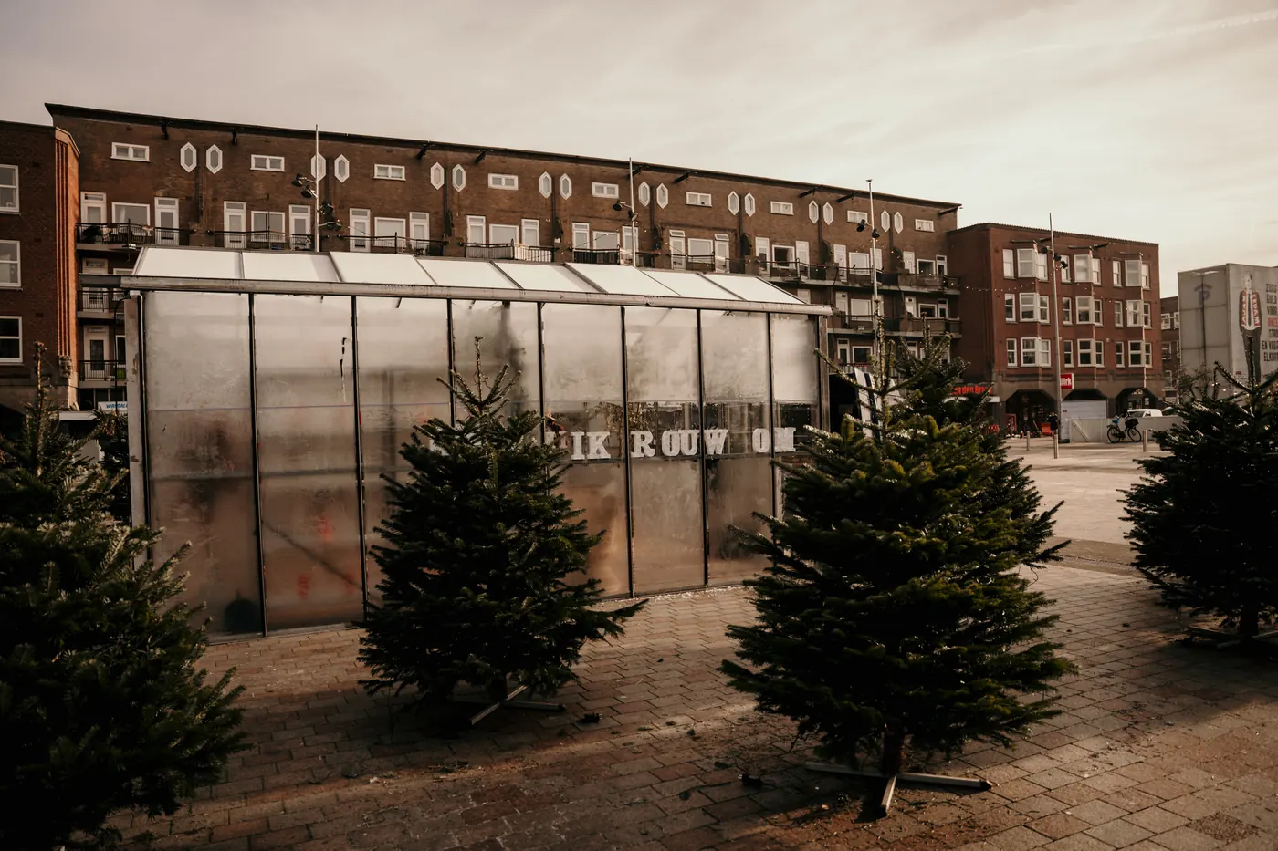 Kas van Rouwen & Vieren op een plein, omringd door kerstbomen